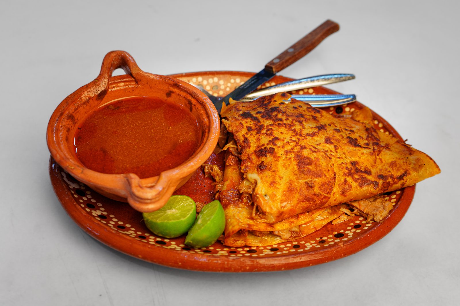 Quesabirria dorada con su consomé en plato de barro