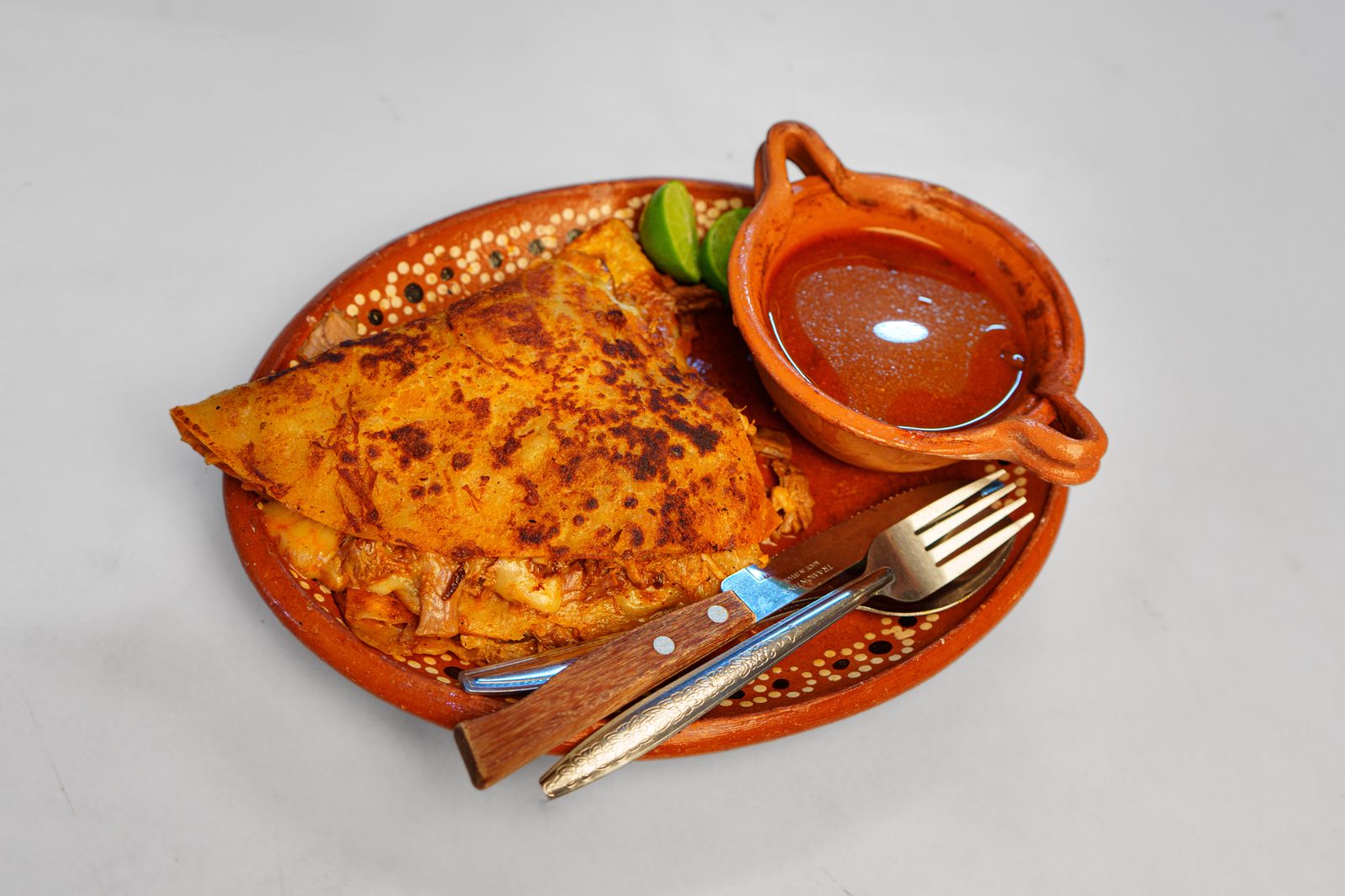 Quesabirria con consomé y limón en plato de barro